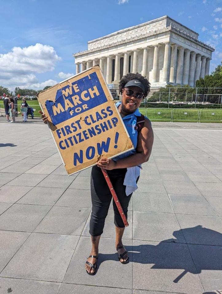 Natalie James holding a historic “We March for First Class Citizenship Now” sign at the Lincoln Memorial